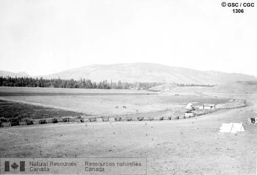 Photo 1306 : Vernon (Colombie-Britannique) vue de l'ouest. (On aperçoit des tentes et des bâtiments de part et d'autre d'une route de terre que longe une clôture  ...