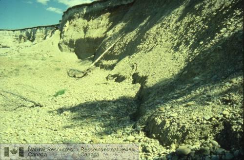 Photo 1999-040B : Escarpement principal du glissement de la pointe Police (environ 10 m de hauteur), exposant la Formation de Cypress Hills. À la base, un petit  ...