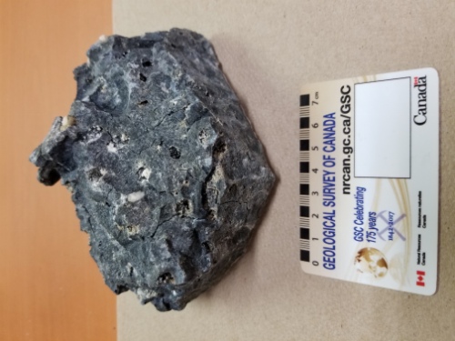 Photo 2020-629: Sample of highly weathered slag consisting of a dark grey, highly vesicular and pervasively cracked material. Some of the vesicles are partially or  ...