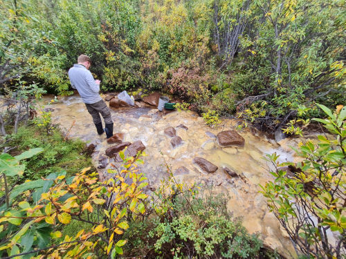 Photo 2022-449 : GSC geologist, Chris Beckett-Brown logging site field data on the tablet after collecting stream sediment samples at site 115J221030 near the Casino  ...