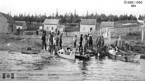 Photo 893 : Pelican Narrows (Saskatchewan). La photo a été prise du quai et montre plusieurs hommes et des canots sur le rivage. À l'arrière-plan, on peut voir  ...