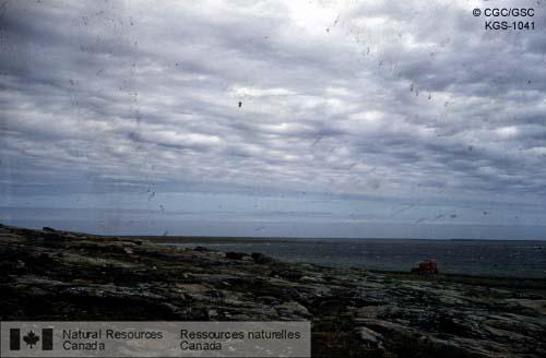 Photo KGS-1041 : Paysage rocheux dénudé, à l'île Cape Jones de la baie d'Hudson. Tracteur et travaux routiers le long du littoral. SNRC 33 et 23 W. (Québec)