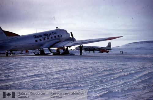 Photo KGS-2 : Un DC-3 et un ARC North Star dans l'arrière plan à Resolute (T.N.-O.), mi-mai 1955.  À noter les skis sur le DC-3